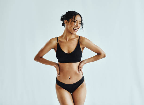 A smiling woman wearing black underwear posing confidently against a light background.